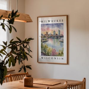 A Milwaukee cityscape print framed and hanging on a beige wall in a cozy dining area, surrounded by wooden furniture and soft indoor lighting.