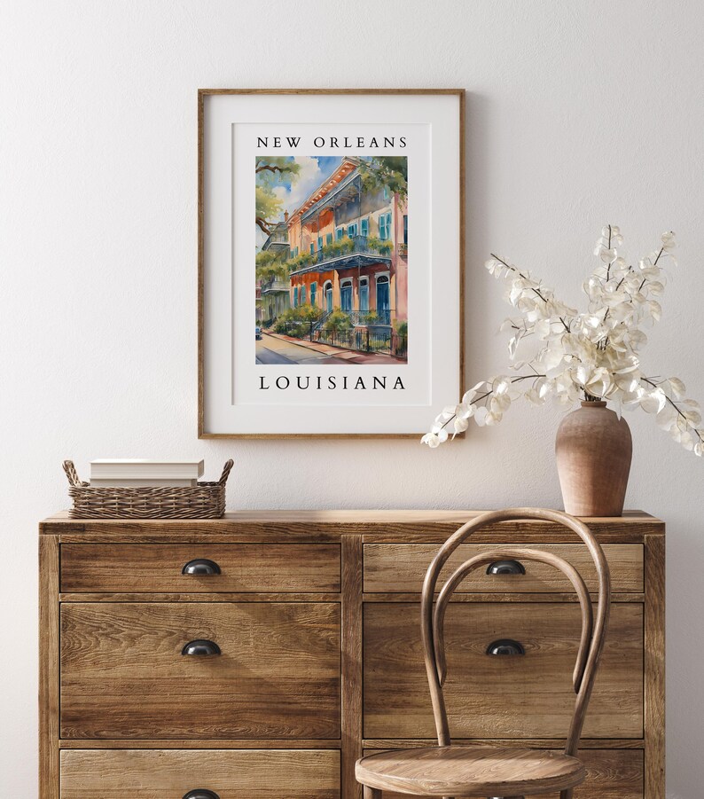 May include: A framed watercolor painting of a colorful building in New Orleans, Louisiana. The building has a balcony and is painted in shades of orange, yellow, and blue. The painting is framed in a light wood frame.