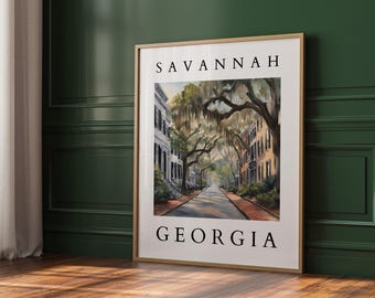 May include: A framed print of a watercolor painting depicting a street scene in Savannah, Georgia. The painting shows a street lined with historic buildings with large oak trees draped in Spanish moss. The text "SAVANNAH GEORGIA" is printed at the top and bottom of the print.