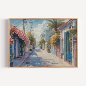 May include: A framed print of a sunlit street scene. The artwork depicts a narrow street lined with buildings in shades of blue and pink, adorned with flowering plants. Palm trees and a bright sky complete the idyllic scene.
