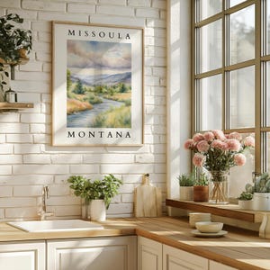 May include: A framed watercolor painting of a river flowing through a valley with mountains in the background. The painting is titled "Missoula, Montana".