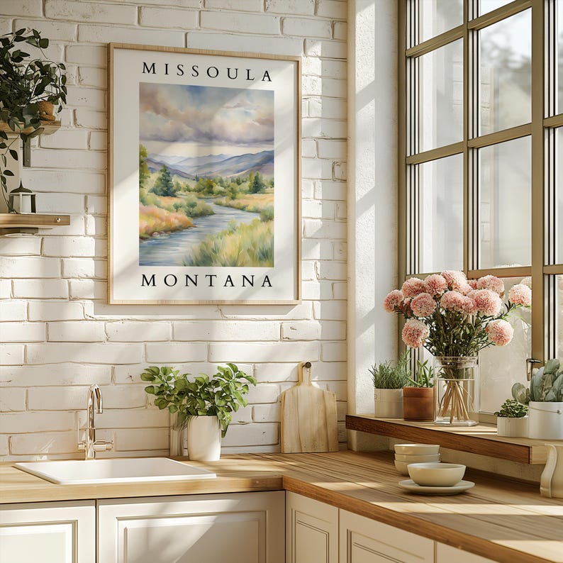 May include: A framed watercolor painting of a river flowing through a valley with mountains in the background. The painting is titled "Missoula, Montana".