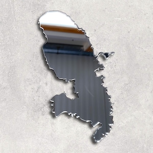 Op de afbeelding: Een zilverkleurige spiegel in de vorm van een geografische omtrek. De spiegel is bevestigd aan een lichtgrijze muur. De randen van de spiegel zijn nauwkeurig gesneden en reflecteren de omgeving.