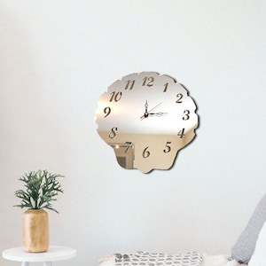 Peut inclure: Une horloge en miroir argenté en forme de coquille avec des aiguilles noires et des chiffres romains.