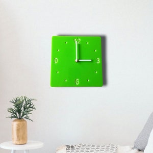 Könnte beinhalten: Eine leuchtend grüne quadratische Uhr mit weißen Zahlen und Zeigern. Die Uhr hängt an einer weißen Wand.