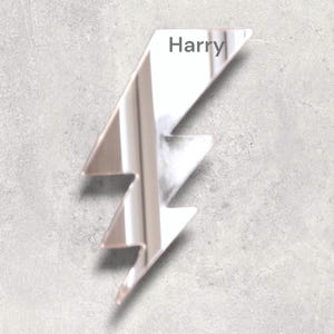 Könnte beinhalten: Ein silberner Blitz in Form eines Spiegels mit dem Namen "Harry" darauf.