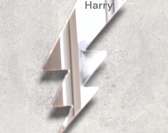 May include: A silver lightning bolt shaped mirror with the name "Harry" written on it.