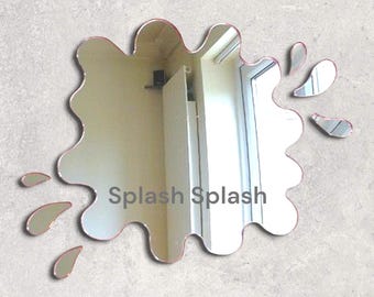 May include: A silver-colored mirror shaped like a paint splatter with the words "Splash Splash" in the center. The mirror has a wavy edge and several smaller splatter shapes around the main shape.