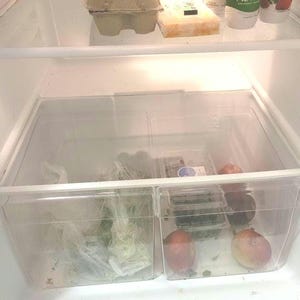 May include: Two clear plastic containers in a refrigerator, one filled with leafy greens and the other with fruit. The fruit includes red apples, green apples, and red plums.