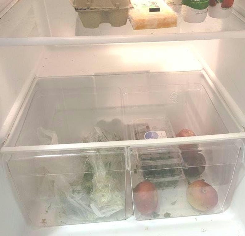 May include: Two clear plastic containers in a refrigerator, one filled with leafy greens and the other with fruit. The fruit includes red apples, green apples, and red plums.