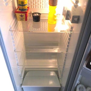 May include: An empty white refrigerator with three glass shelves and a clear plastic container in the bottom. The refrigerator has a light on inside and a yellow bottle on the top shelf.