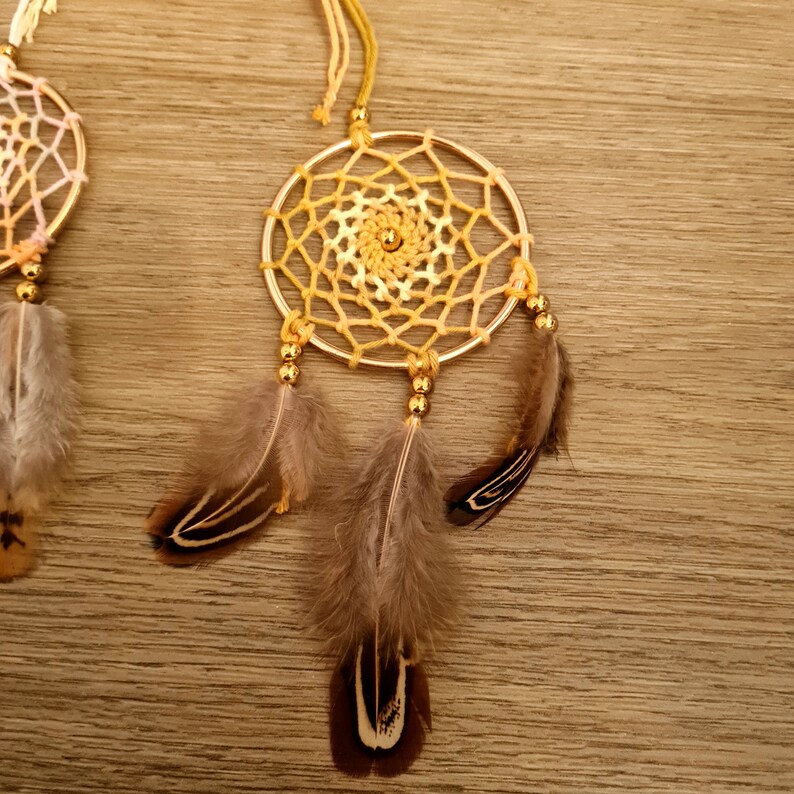 May include: A gold dream catcher with a yellow and white crocheted web and three brown feathers.
