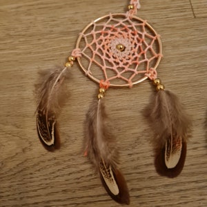 May include: A pink and orange dreamcatcher with brown feathers and gold beads.