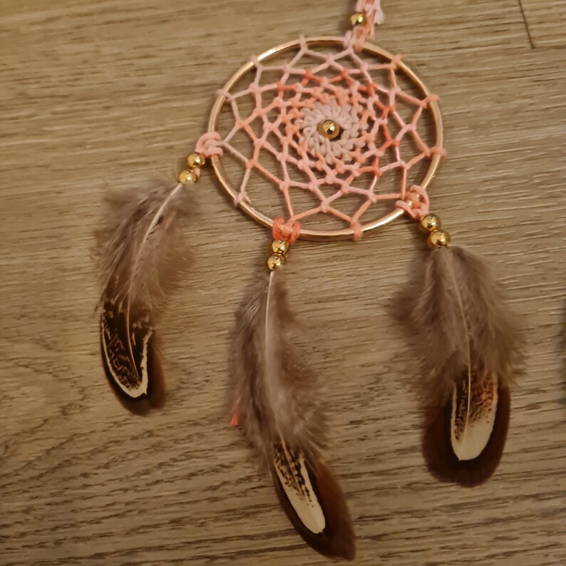 May include: A pink and orange dreamcatcher with brown feathers and gold beads.