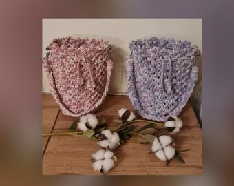 May include: Two crocheted bags with a drawstring closure. One bag is pink and white, the other is purple and white. The bags are sitting on a wooden surface with cotton bolls.