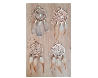 May include: Four handmade dream catchers with woven circular webs and hanging feathers. The dream catchers are in shades of beige and white, with feathers in neutral tones. They are displayed on a light brown wooden surface.