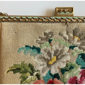 Puede incluir: Un bolso de mano vintage bordado con flores con un marco de metal dorado y un ribete de esmalte azul claro. El bolso presenta un diseño floral con flores blancas, rosas, verdes y amarillas.