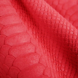 Peut inclure: Gros plan sur un tissu rouge &agrave; texture de peau de serpent. Le tissu pr&eacute;sente un motif en relief textur&eacute; qui ressemble &agrave; des &eacute;cailles de serpent.