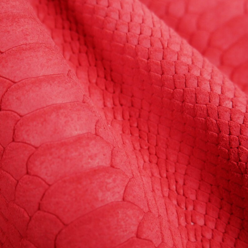 Peut inclure: Gros plan sur un tissu rouge &agrave; texture de peau de serpent. Le tissu pr&eacute;sente un motif en relief textur&eacute; qui ressemble &agrave; des &eacute;cailles de serpent.