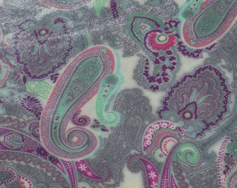 May include: Close-up of a fabric with a paisley pattern. The design features large, teardrop-shaped motifs in shades of grey, purple, pink, and teal, set against a cream-coloured background. The fabric has a subtle shimmer, enhancing the intricate details.