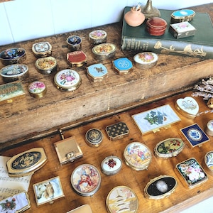 Puede incluir: Una colección de numerosas cajas decorativas pequeñas de diversas formas, incluyendo redondas, ovaladas, cuadradas y rectangulares. Las cajas presentan diversos diseños como motivos florales, escenas de paisajes, retratos y patrones geométricos.