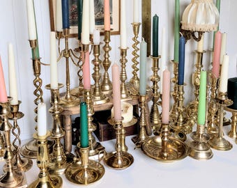 Peut inclure: Une collection de bougeoirs en laiton de différentes hauteurs et designs, avec des tiges torsadées, cannelées et lisses. Les bougeoirs portent des bougies effilées aux couleurs blanc, rose, vert, bleu et pêche, avec un petit abat-jour.