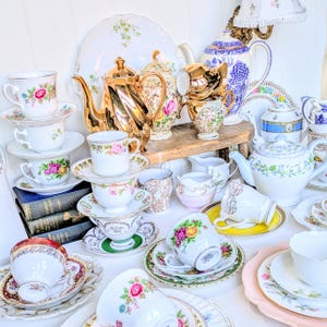 Könnte beinhalten: Eine Sammlung von Vintage-Teetassen, Untertassen und Teekannen in verschiedenen Blumenmustern und Farben. Die Teetassen und Untertassen sind übereinander gestapelt, und die Teekannen sind auf einem Holzregal angeordnet. Es gibt auch mehrere Milchkännchen und Zuckerdosen auf dem Bild.