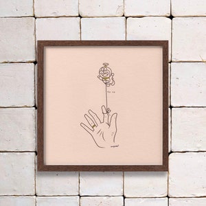 May include: A framed art print featuring a cartoon character holding a string that is tied to a finger. The artwork is in a minimalist style with black line art on a light pink background. The text "Yo yo" is below the character.