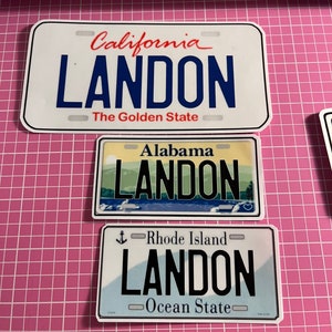 May include: Three license plate stickers with the name "LANDON". The top sticker is from California, the middle from Alabama, and the bottom from Rhode Island. Each plate has a different background and design.