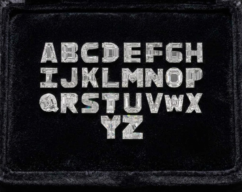 May include: A full alphabet of sparkling, clear gemstone letters, each with a unique faceted design, arranged on a black velvet surface. The letters are evenly spaced and presented in a neat, organized display.