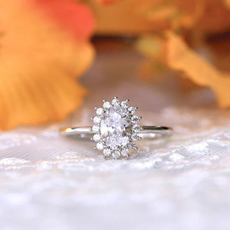 May include: A silver ring with an oval-shaped diamond surrounded by a halo of smaller diamonds.