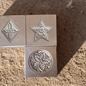 Könnte beinhalten: Drei Metall-Ausstecher mit verschiedenen Designs: eine Raute mit einem Blumenmuster, ein Stern mit einem Blumenmuster und ein Kreis mit einem Blumenmuster.