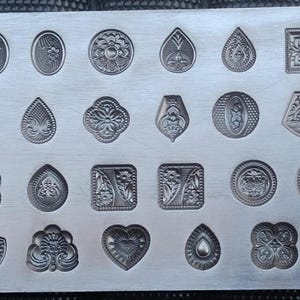 May include: A metal mould with 28 different designs for making jewellery or other crafts. The designs include hearts, flowers, leaves, and geometric shapes.