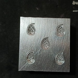 May include: A metal block with five teardrop-shaped designs, each with intricate details. The designs are evenly spaced on the block.