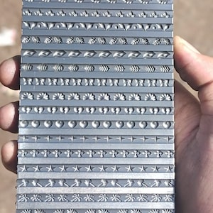 Könnte beinhalten: Eine Metallplatte mit 18 verschiedenen dekorativen Bordüren. Die Platte wird in einer Hand gehalten.