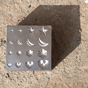May include: A silver metal stamp with various designs including stars, crescent moons, clover shapes, and hearts.