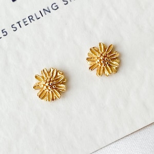 Peut inclure: Une paire de boucles d'oreilles clous en forme de marguerite en argent sterling doré. Les boucles d'oreilles sont sur une carte blanche avec le texte "INA 925 STERLING SILVER".
