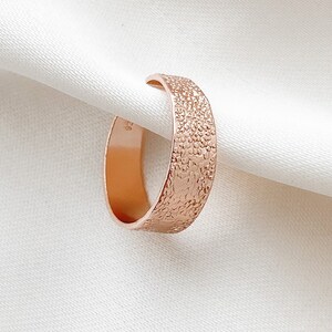 Könnte beinhalten: Ein roségoldener Ring mit einer strukturierten Oberfläche. Der Ring ist dick und hat eine abgerundete Form.