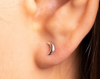 Könnte beinhalten: Nahaufnahme eines Ohrs mit einem kleinen Halbmond-Ohrring. Der Ohrring ist silberfarben und wird am Ohrläppchen getragen.
