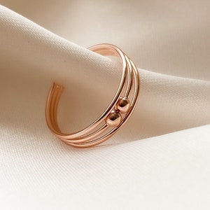 Könnte beinhalten: Ein Ring aus Roségold mit drei Bändern und zwei kleinen Perlen.