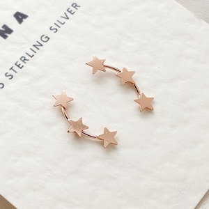 May include: A pair of gold-toned sterling silver earrings featuring a curved line of five star shapes.