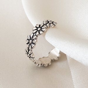May include: A silver ring featuring a delicate design of small flowers around the band.