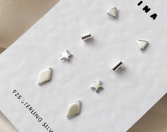 Könnte beinhalten: Ein Set mit sechs silbernen Ohrringen in verschiedenen Formen, darunter Sterne, Diamanten und Dreiecke. Die Ohrringe werden auf einer weißen Karte mit dem Text "INA" und "925 STERLING SILVER" präsentiert.