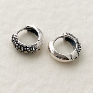 Könnte beinhalten: Ein Paar silberne Creolen mit einem strukturierten Design. Die Ohrringe sind aus Silber und haben eine kleine, runde Form.