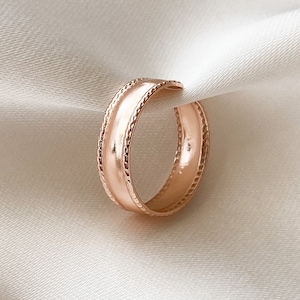 Könnte beinhalten: Ein Ring aus Roségold mit einem strukturierten Band. Der Ring ist schlicht und elegant.
