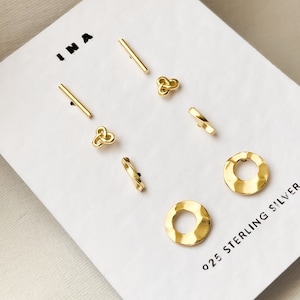 May include: A set of six gold-toned sterling silver earrings. The earrings include two pairs of small circles, two pairs of small knots, and two pairs of small bars.