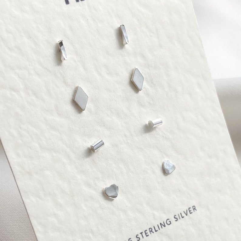May include: A set of six sterling silver stud earrings in various shapes, including a heart, a diamond, and a rectangle. The earrings are displayed on a white card with the text "Sterling Silver".