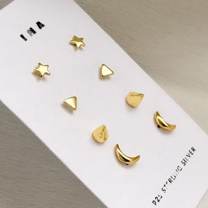 Könnte beinhalten: Ein Set goldfarbener Ohrstecker in verschiedenen Formen, darunter Sterne, Dreiecke, Tropfen und Halbmonde. Die Ohrringe werden auf einer weißen Karte mit dem Text "925 STERLING SILVER" präsentiert.