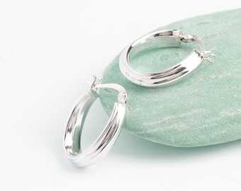 Puede incluir: Un par de pendientes de aro de plata con un diseño acanalado. Los pendientes están sobre una piedra verde claro.