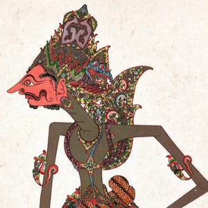 Op de afbeelding: Gedetailleerde illustratie van een traditionele Indonesische Wayang Kulit-pop. De pop heeft een rood gezicht, een uitgebreide hoofdtooi en sierlijke kleding met ingewikkelde patronen in tinten rood, groen en bruin. Het profiel van de pop is zichtbaar.